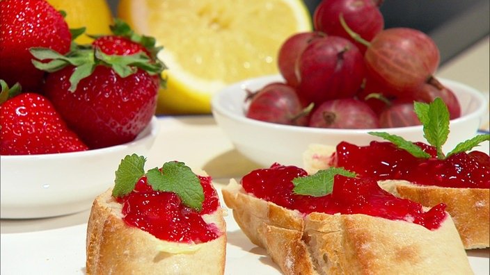 Baguettescheiben mit rotem Fruchtaufstrich. Im Hintergrund Stachel- und Erdbeeren.