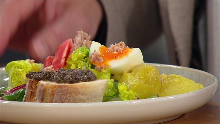 Ein Salat Nicoise und ein Baguette mit Oliventapenade auf einem weißen Teller