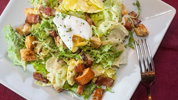Ein Salade Lyonnaise mit pochoertem Ei und Croutons auf einem weißen Teller