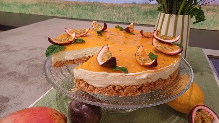 auf einer Glasplatte steht ein hübsch dekorierter runder Kuchen, Obenauf liegen ein paar Maracujastücke.