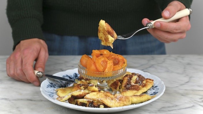 Zwei Hände essen mit Messer und Gabel Kaiserschmarrn mit Aprikosen.