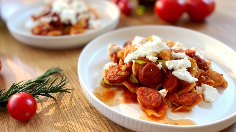 Nudeln, Chorizo-Würstchen und rote Soße wurden gemischt auf einem Teller drapiert.