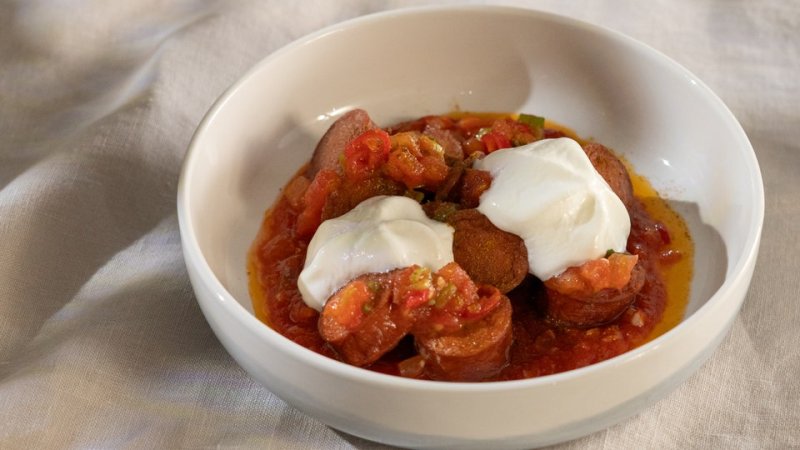 Geschnitte Currywurst mit Soße in einem tiefen Teller. Darauf ein Klecks Sauerrahmschaum.
