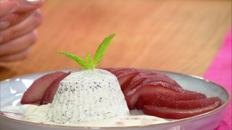 Ein helles Mohnparfait in Törtchenform. Daneben eine eingelegte rote Birne in Scheiben geschnitten. Garniet mit einem Minzblättchen.