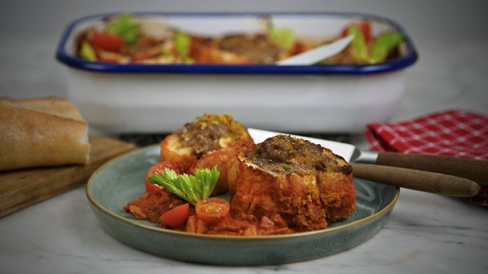Zwei große Frikadellen liegen auf einem Teller. Im Hintergrund steht die Ofenform, in der der Rest der Mahlzeit liegt.