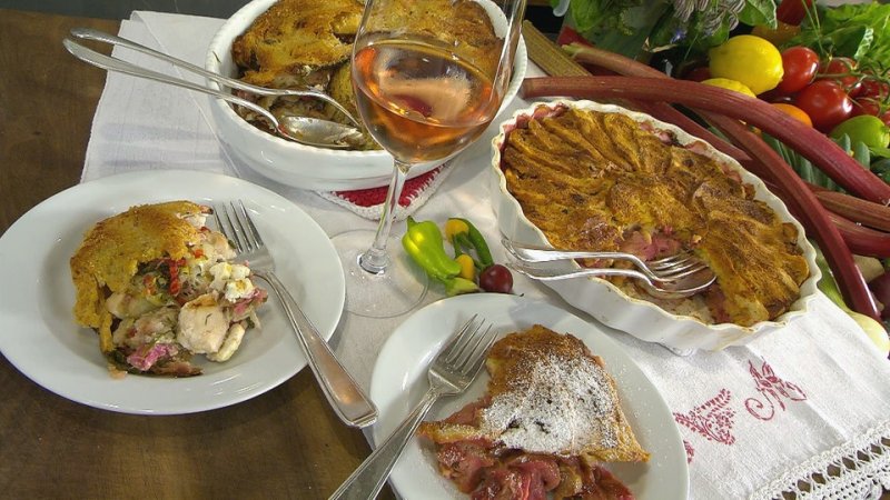Gratin aus Rhabarber und Hähnchen in einer Auflaufform. Daneben Teile des Gratins auf zwei Teller verteilt und ein Glas Wein in der Mitte.